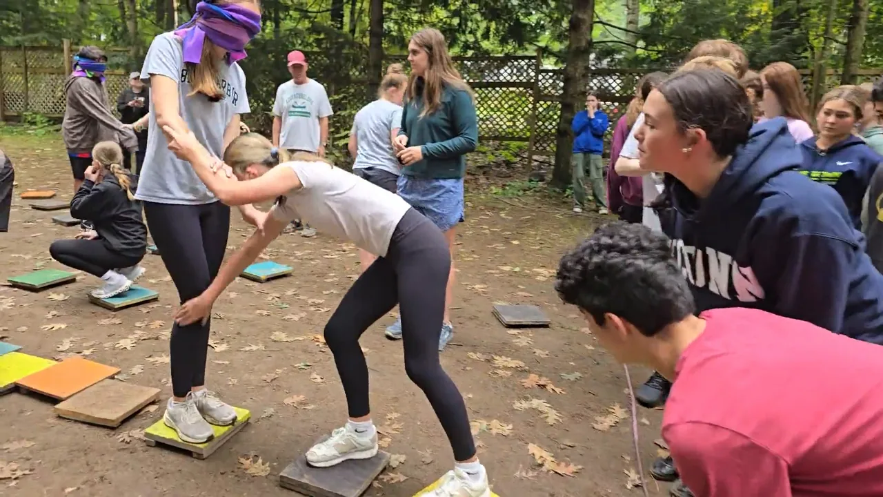 Students supporting and guiding a peer through an outdoor group challenge