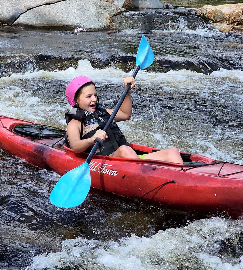 A camper paddling a kayak through whitewater